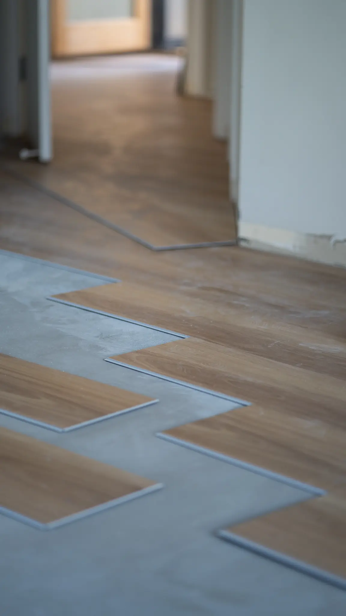 Staggered boards being laid across a prepared concrete slab in a hallway