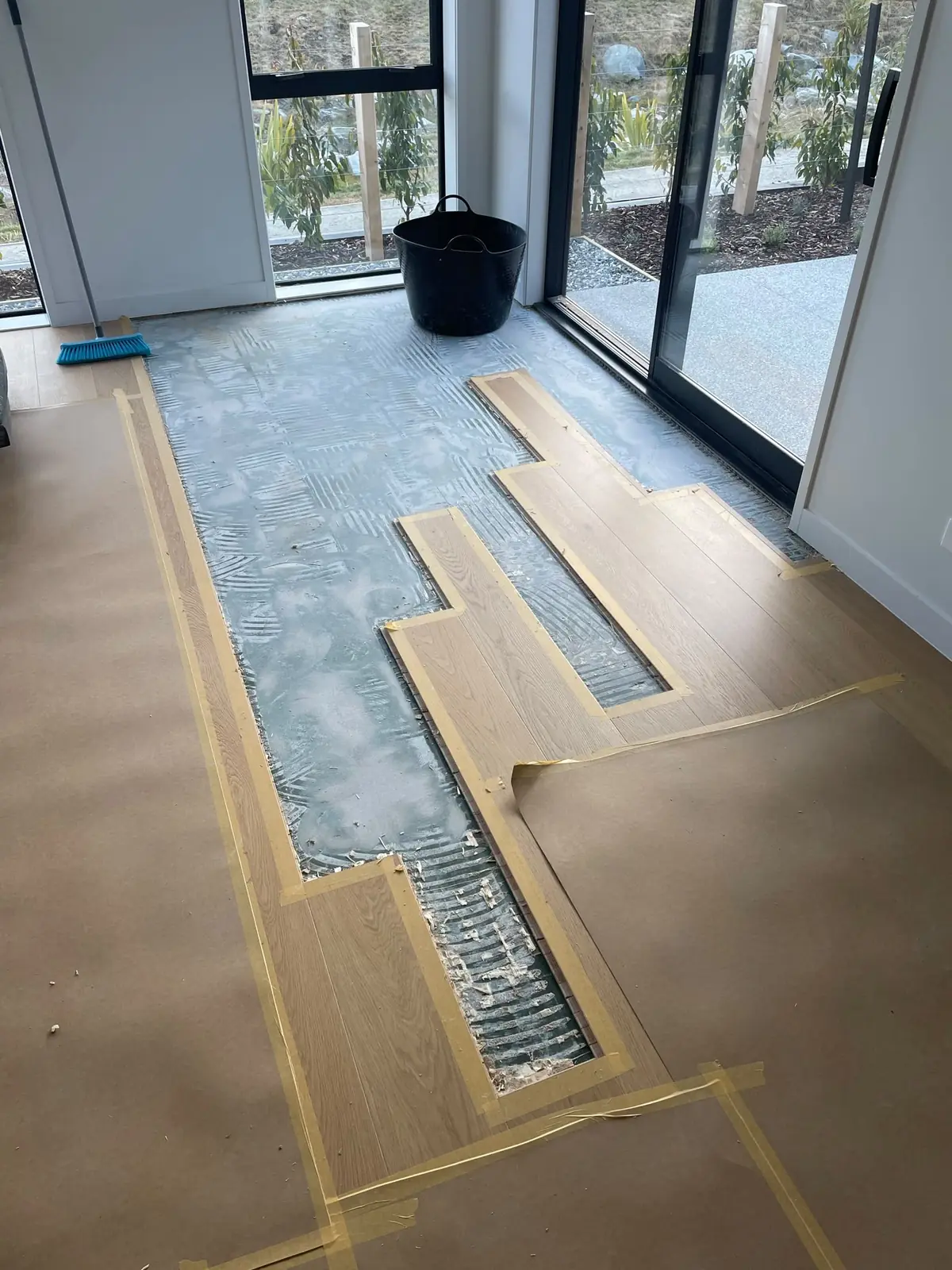 Timber boards being glued down over trowelled adhesive, with protective paper over the finished section