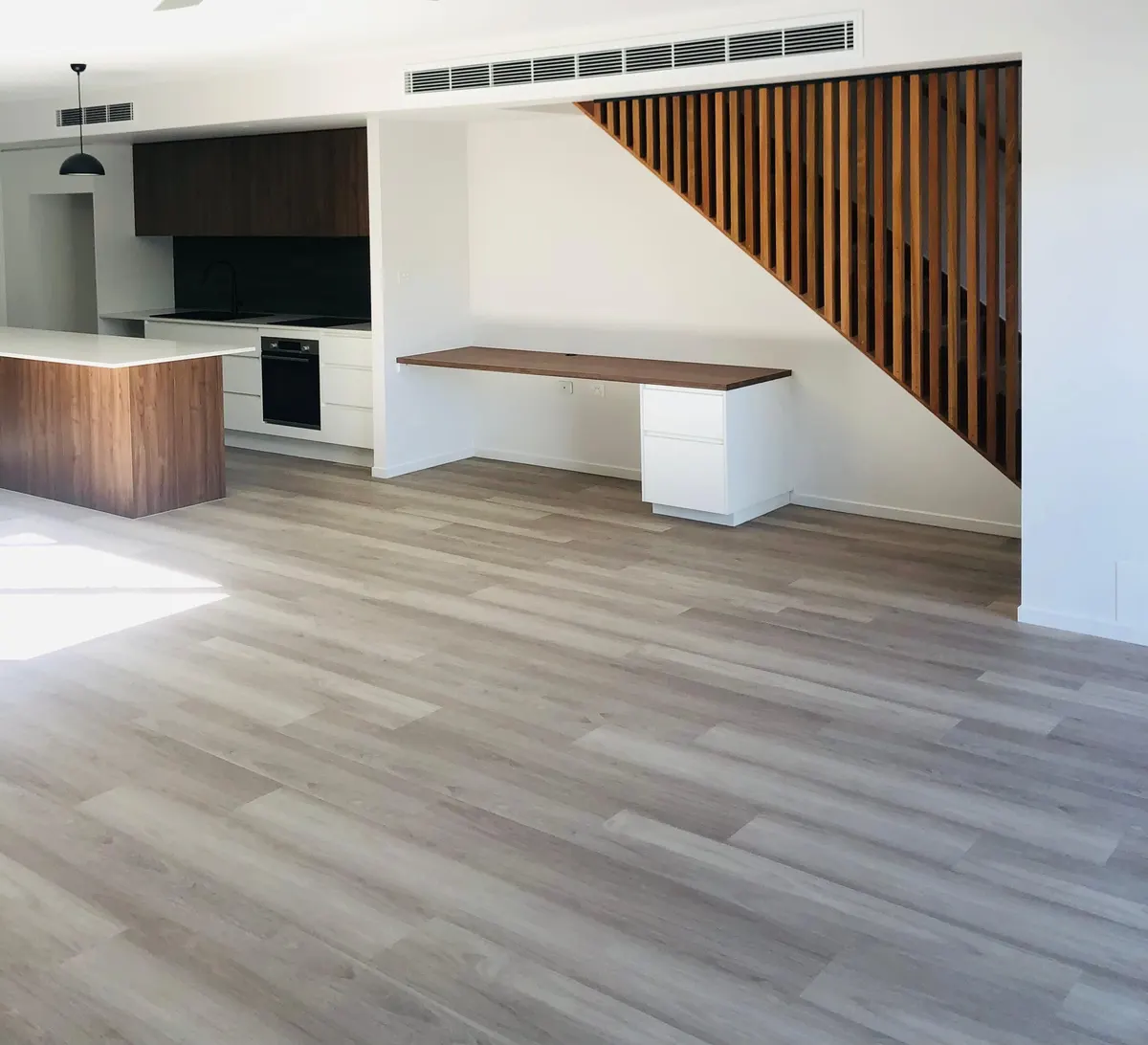 Hybrid flooring through a kitchen and living area beside a timber batten stair screen