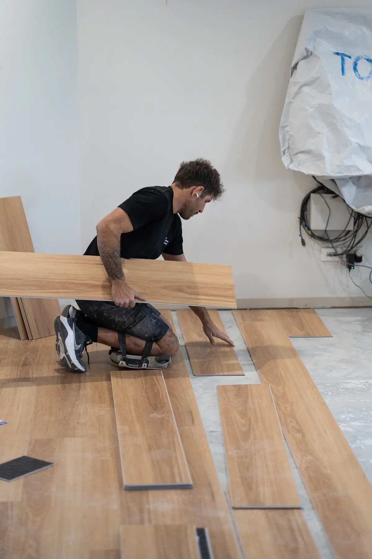 Installer carrying a long plank across a partly laid floor