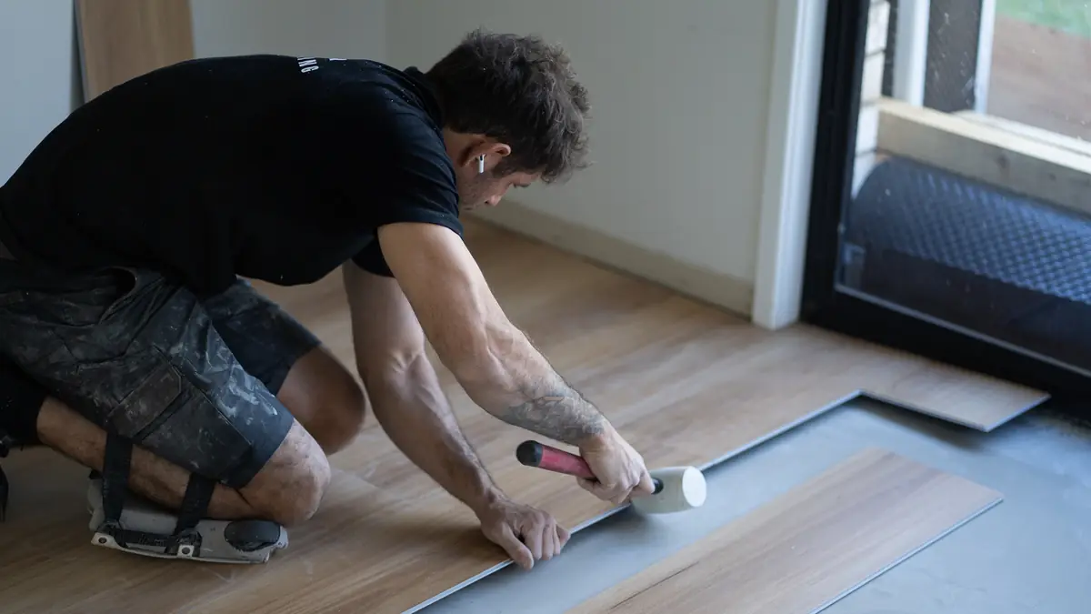Installer tapping boards together with a rubber mallet beside a sliding door