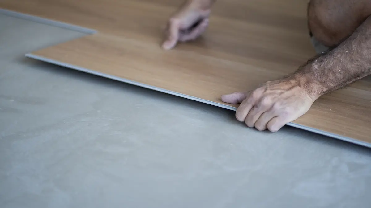 Installer’s hands aligning a wood-look plank over a prepared concrete slab